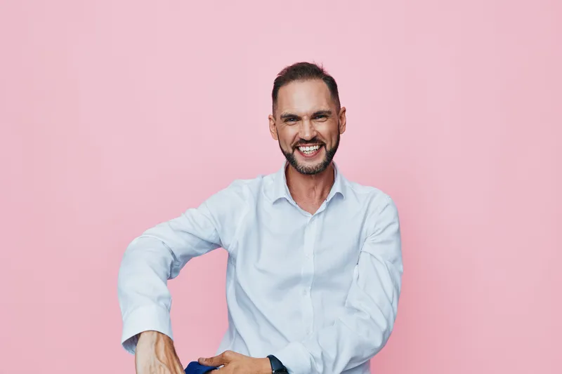 A confident business professional man smiles warmly against a solid pink backdrop, projecting approachable leadership and positive emotion in a clean, isolated color setting.