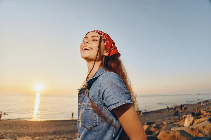 lifestyle woman enjoying sunset in modern boho-western denim street style with warm film color tones and carefree joyful expression near beach shore