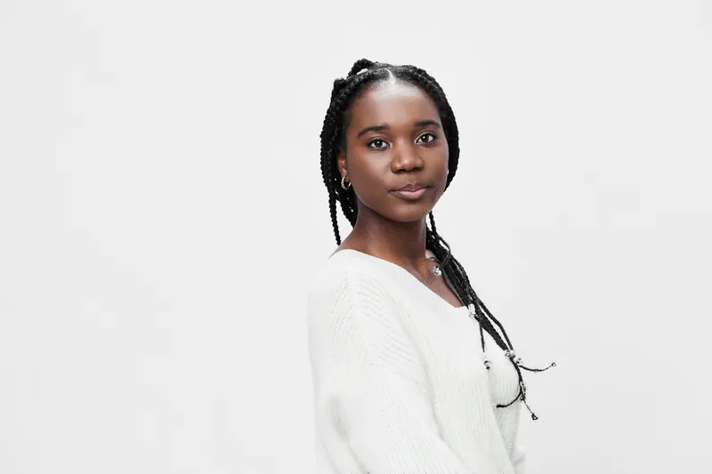 Confident young woman with braided hair, wearing a cozy white sweater, against a minimalistic white background, showcasing self assurance, elegance, and style