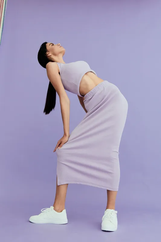 tall woman in lilac dress posing fashionably against pastel purple background, showcasing modern style, casual footwear, and graceful posture in studio lighting.
