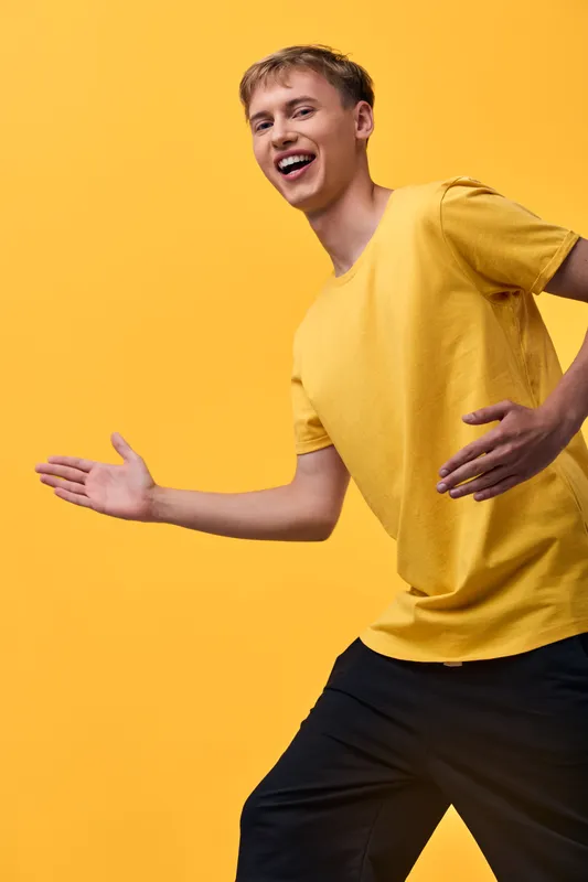 Joyful movement of a dancer in a bright yellow shirt against a solid yellow backdrop, conveying energy, playfulness, and optimism in a casual, upbeat scene.