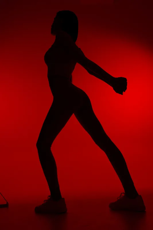 Silhouette of a woman sport fitness stretching her arms and legs against a vibrant red background, showcasing strength, balance, and flexibility for active lifestyle.