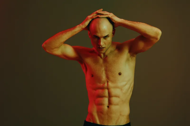 Athletic man posing with a strong posture, emphasizes strength and confidence, captured in a dramatic light setting. The image features a vibrant color contrast.