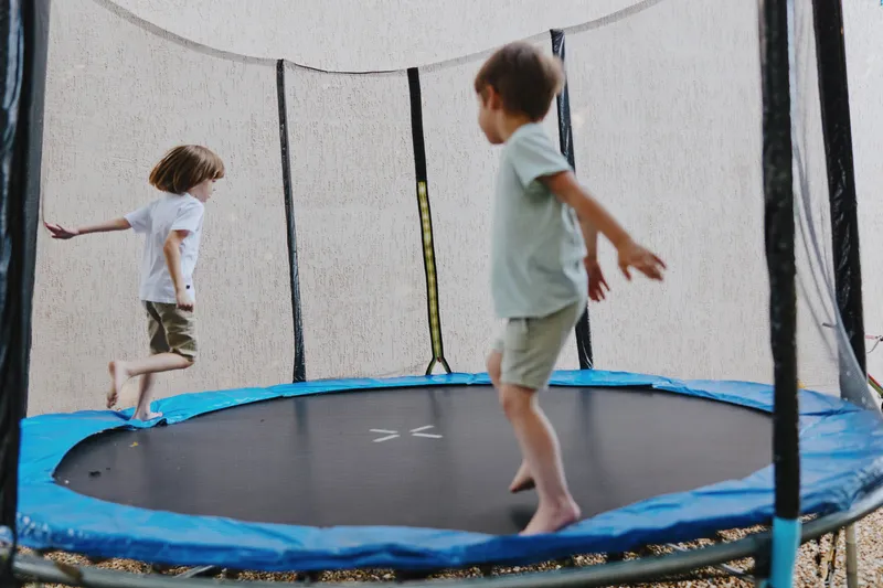 Two energetic boys joyfully bouncing on a trampoline, showcasing playfulness and fun in a vibrant outdoor setting. Perfect for capturing childhood delight.