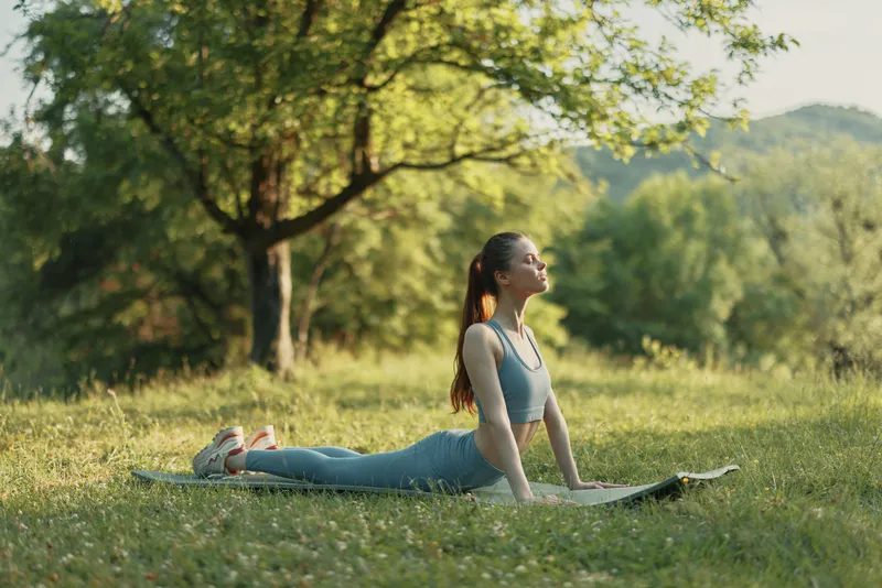 Young woman practicing yoga outdoors in a lush green park, wearing a stylish light blue outfit, radiating calmness and tranquility during a sunny day