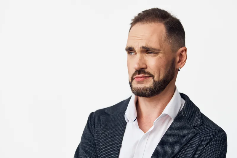 A business professional man stands against an isolated colored background, conveying focus and confidence through a thoughtful gaze and composed posture.
