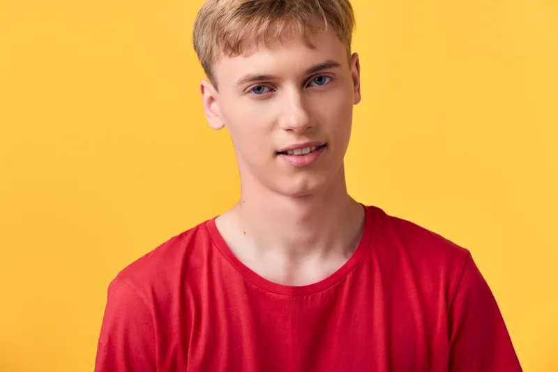 Close up of a young man in a red shirt against a bright yellow background, casual and smiling, showcasing a modern fashion vibe, studio lighting, clean silhouette and approachable lifestyle for