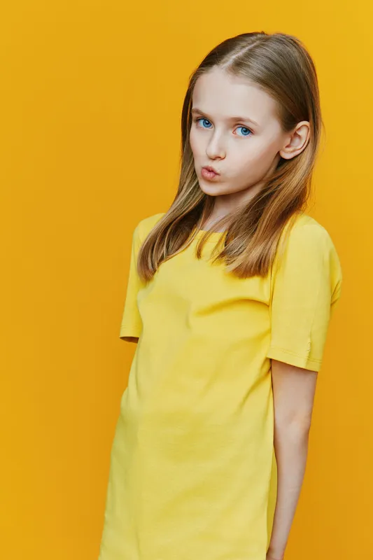 Young girl with long hair in a yellow t shirt, expressing a playful attitude against a vibrant yellow backdrop, showcasing a cheerful and energetic concept