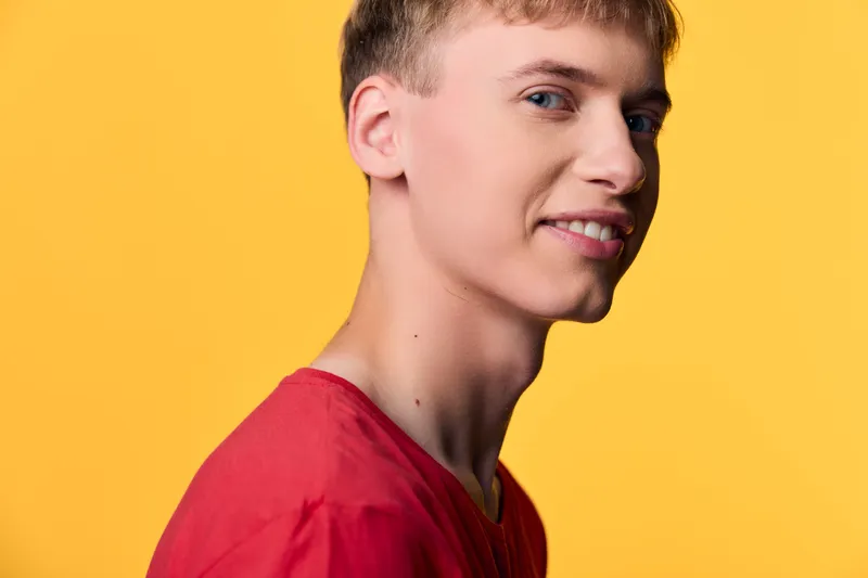 Young man in red shirt against a bright yellow background, smiling softly in a studio setting, clean composition for lifestyle, fashion or product visuals
