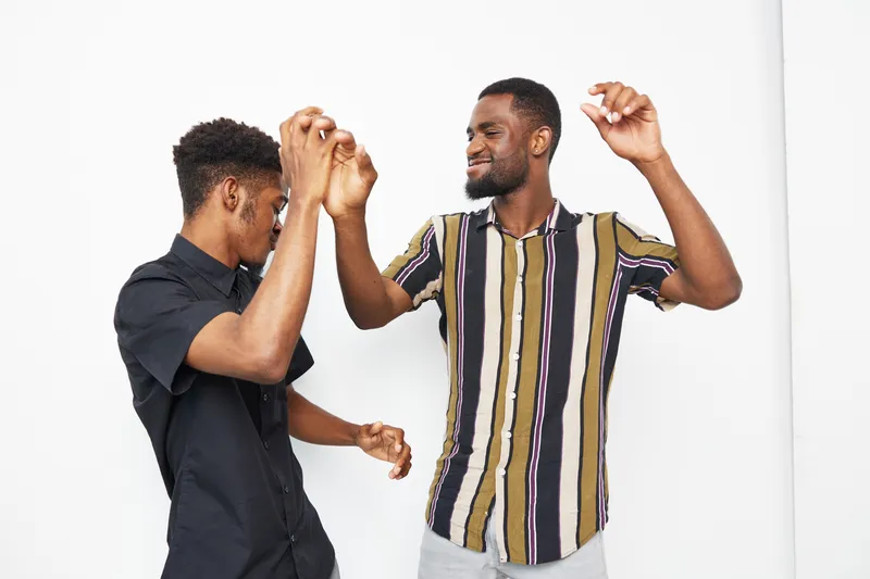 Two black men enjoying a joyful moment together, dancing with enthusiasm against a clean, white backdrop. Their playful expressions capture the essence of celebration.