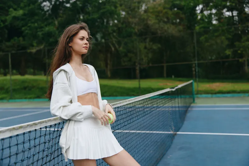 Young female tennis player in sporty outfit poses on tennis court, showcasing athleticism and confidence, with a vibrant green background and seasonal sports energy