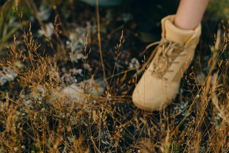 One person steps through dry grass in a sunlit outdoor scene, a beige boot close to the ground, conveying a calm moment of exploration and connection with nature, natural colors, soft breeze