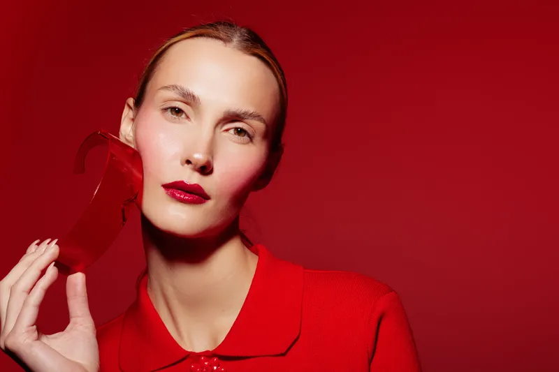 Portrait of a woman with red lipstick and red outfit holding a red object on a red background. Concept of fashion, beauty, and monochrome style with bold makeup and color.