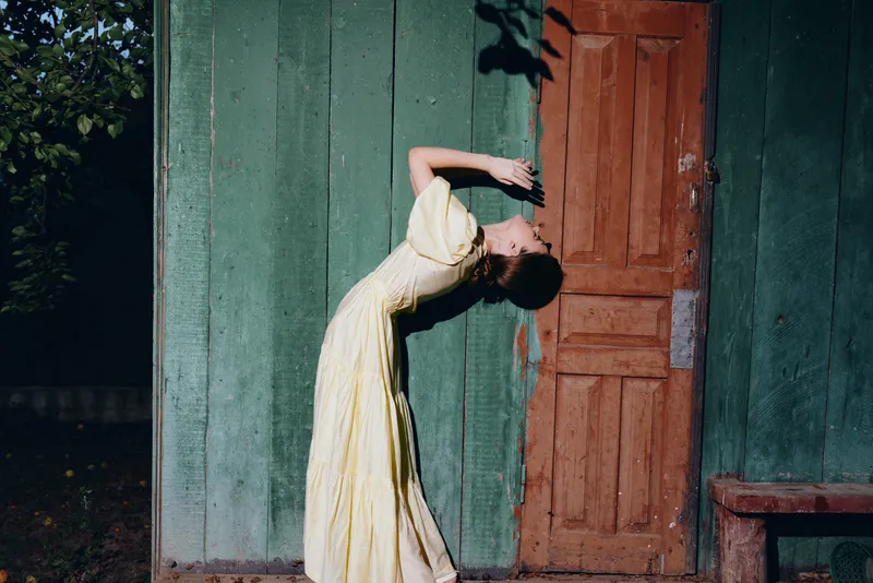 Woman in yellow dress leaning against vintage wooden door authenticity inclusivity portrait rustic texture