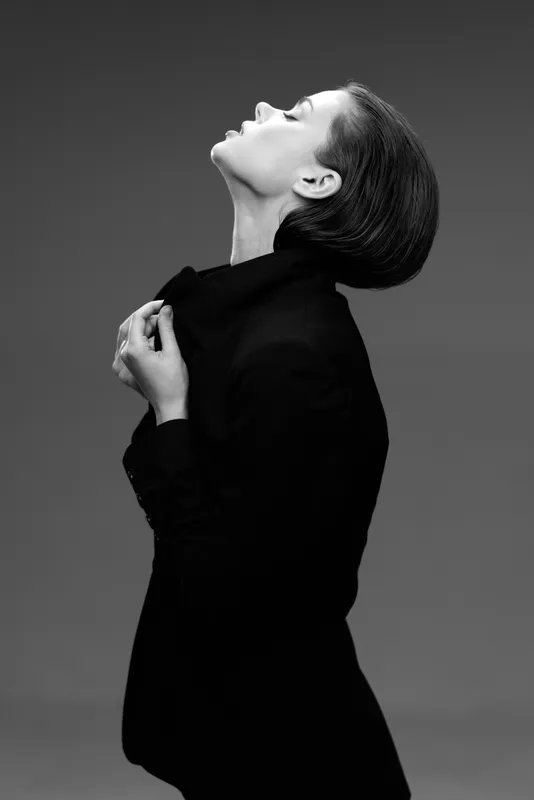 Black and white portrait of a stylish woman with short hair wearing a dark jacket in a thoughtful pose.