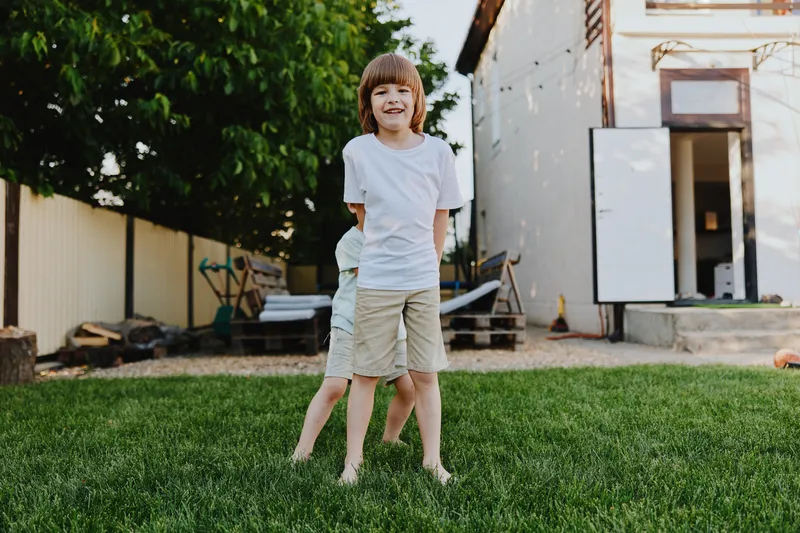 Happy boy playing outdoors in the garden, enjoying a sunny day with friends, wearing casual clothes and barefoot in a relaxed atmosphere.