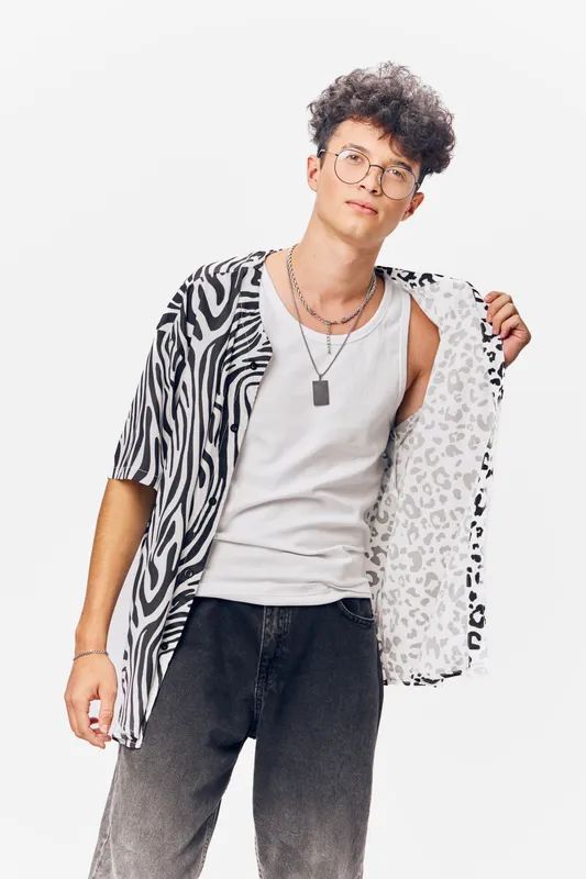 young man wearing trendy zebra print shirt and white tank top posing confidently with glasses against white background, casual style, urban fashion