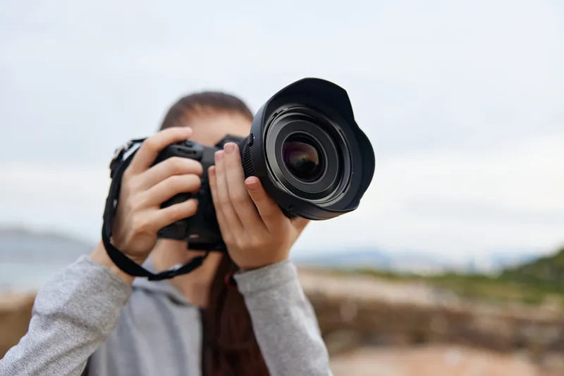 A young woman capturing photographs with a DSLR camera against a blurred natural background, showcasing her passion for photography in a serene environment