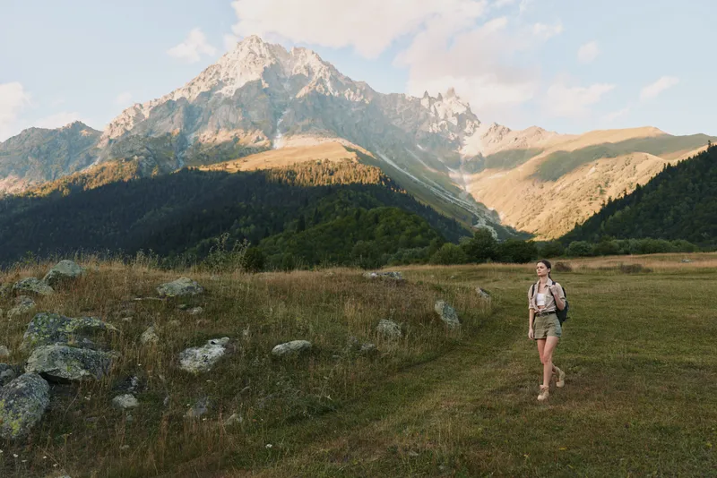 Woman hiking in nature, walking on grassy trail, mountain landscape background, clear sky, casual outfit, outdoor activity, adventurous mood
