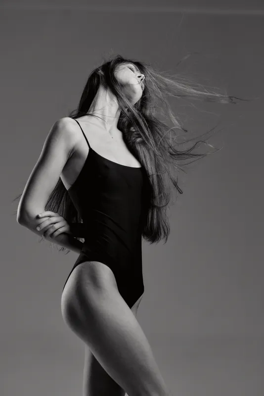 Black and white artistic portrait of a woman in a leotard with flowing hair in motion