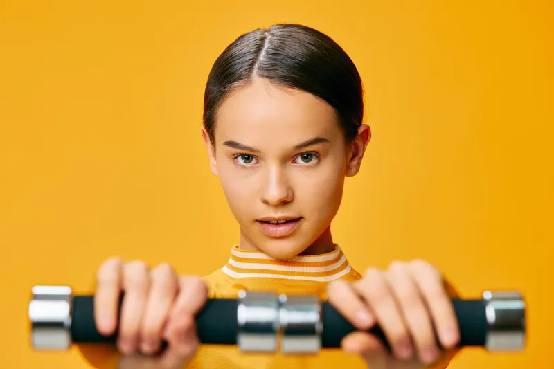 Woman fitness, sport themed portrait with dumbbells, close up grip and determined expression, bright orange background, workout routine, strength training and athletic attitude in a modern gym vibe.