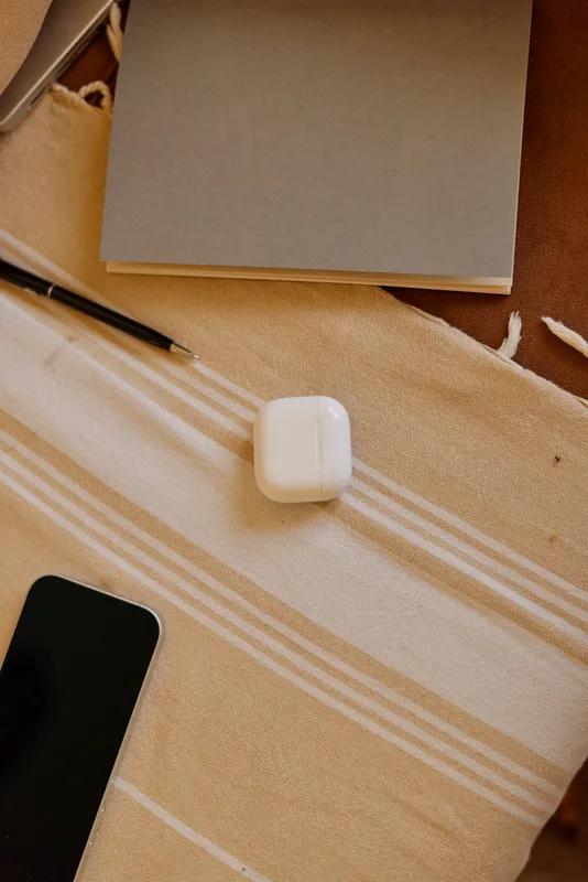 Casual home desk scene with a smartphone and a small white accessory on striped fabric, relaxed mood, soft lighting, everyday clutter, cozy atmosphere, natural tones, warm textures, organized calm