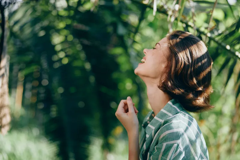 woman enjoying outdoor scenery, portrait in natural light, serene mood and joyful smile, lush greenery and sunlit background creating a calm, candid moment in nature