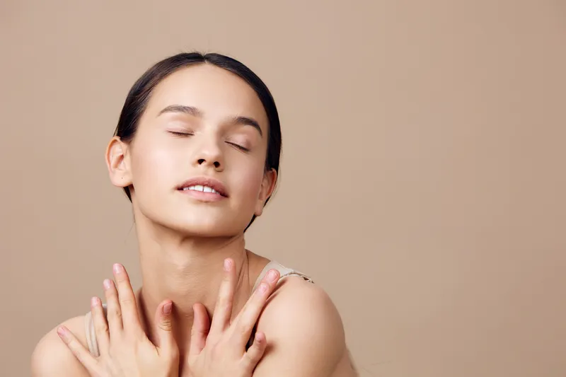 Serene young woman with closed eyes, wearing minimal makeup and soft clothing, embracing relaxation against a warm beige background