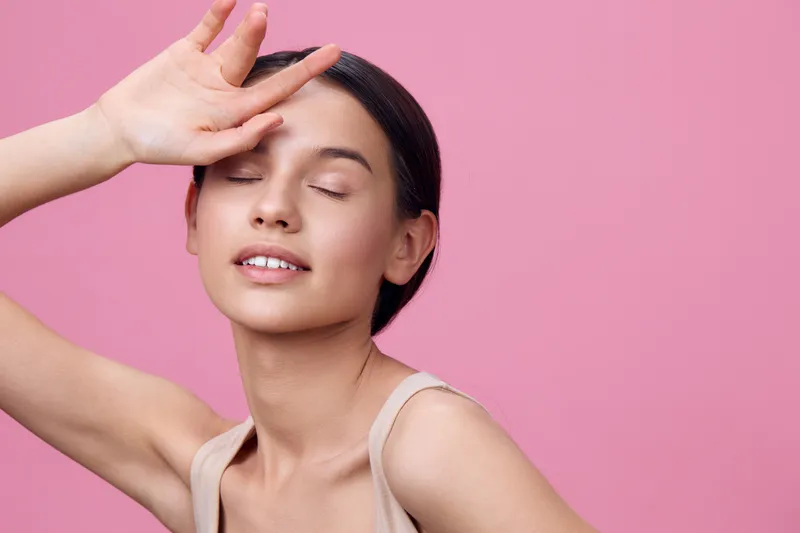Young woman with closed eyes and a serene expression on a pink background, wearing a light beige top, conveying peace and tranquility through natural beauty