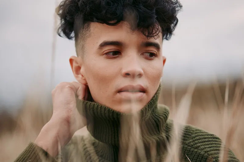 A candid portrait of a young person in a knit turtleneck, captured in natural light with an honest expression, conveying authenticity and credibility in everyday style.