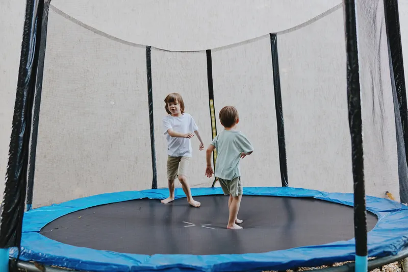 Two joyful boys playing on a trampoline, enjoying a sunny day, surrounded by a vibrant outdoor setting, showcasing fun and excitement in childhood.