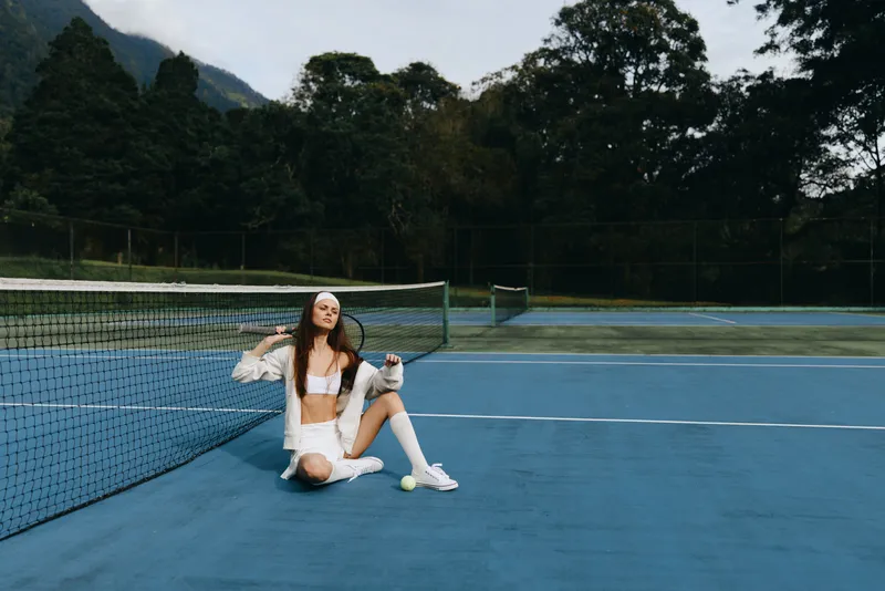Young woman playing tennis on a blue court, wearing sporty white outfit and headband, exuding joy and confidence in a vibrant outdoor setting