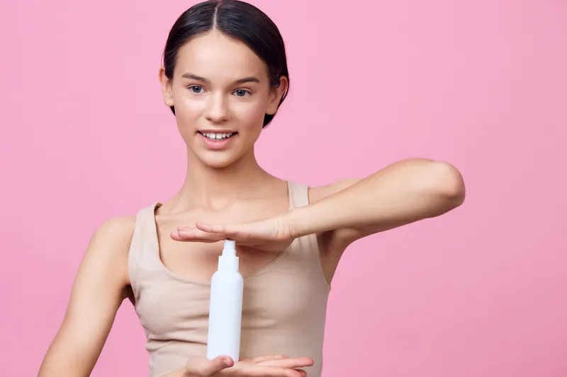 Young woman showcasing a skincare product against a pink background, promoting beauty and self care with confidence and joy