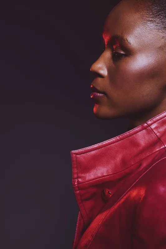 Profile of a dark skinned African woman wearing a red leather jacket on black background. Concept of fashion, beauty, elegance, and confident female portrait in studio lighting.