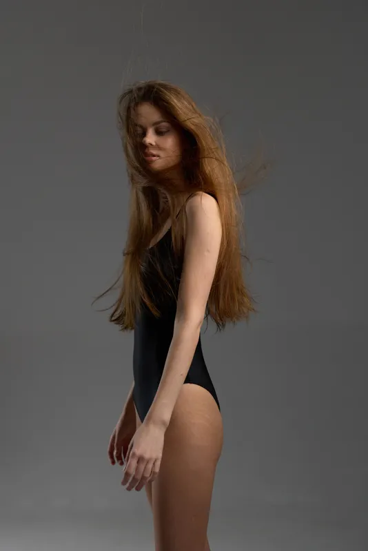 young woman with long hair wearing black bodysuit posing against gray background