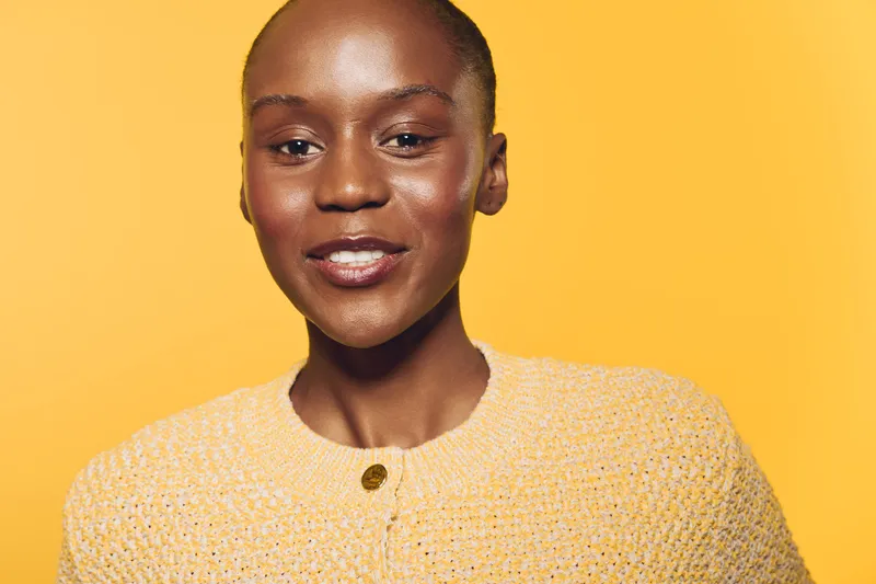 Confident African woman with dark skin smiles wearing a yellow knitted sweater on a bright yellow background. Portrait of natural beauty, positive mood, and fashion concept.