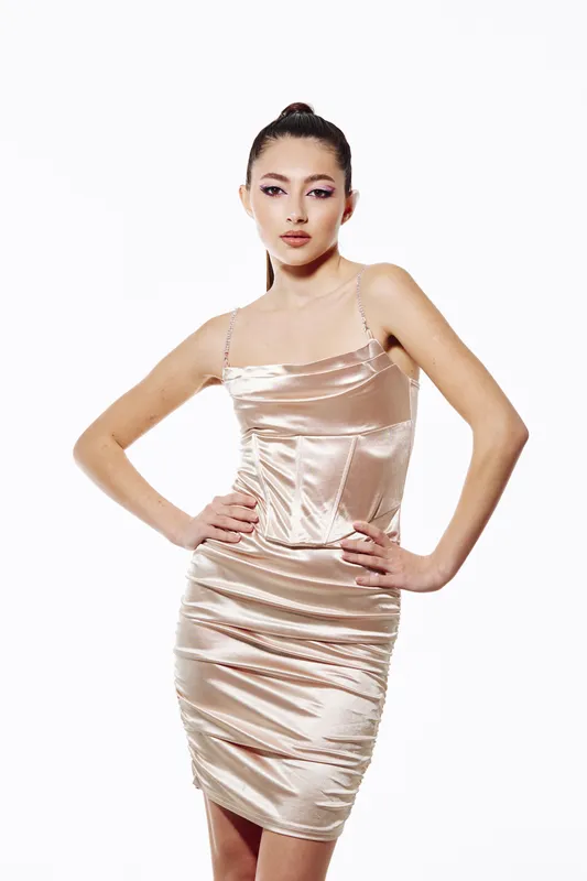 Slim woman with elegant poise wearing champagne satin dress and high ponytail on white background. Concept of beauty, fashion, style, and creative modeling.