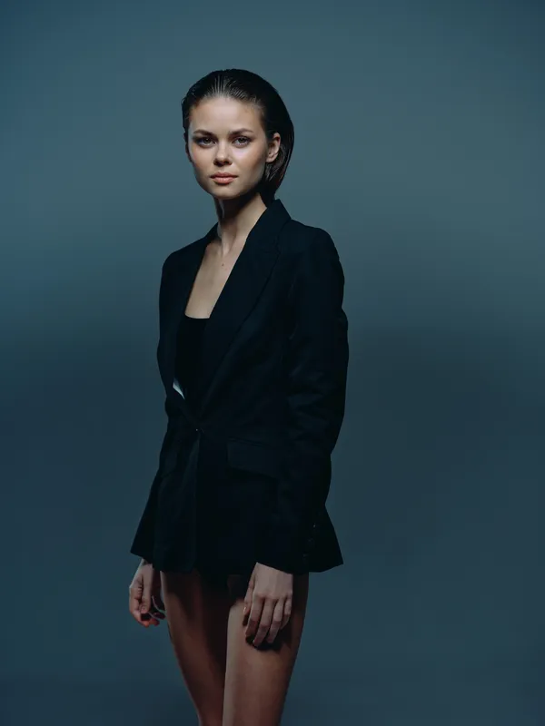 Serious woman in black blazer posing with confident look against dark blue background