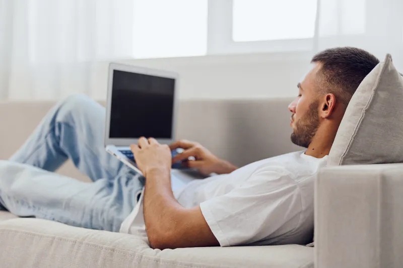 Relaxed man working on a laptop at home, showcasing a modern lifestyle with cozy decor and natural light, embodying productivity and comfort in daily life.