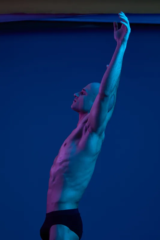 Athletic man with outstretched arms posing against a colorful blue background, showcasing strength and expression. Ideal for fitness and wellness themes.