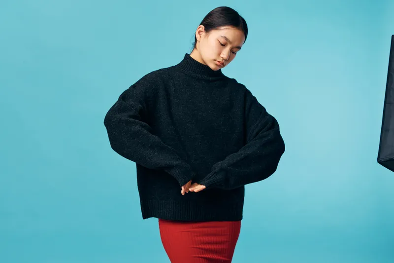 Young woman wearing black sweater and red skirt posing with eyes closed on blue background. Fashion, portrait and casual style with minimalist studio light for clothing model.