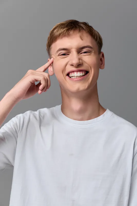 Smiling man in a white tshirt touches his temple signaling a moment of insight and creativity in a clean studio setting ideal for ideas motivation and positive thinking topics