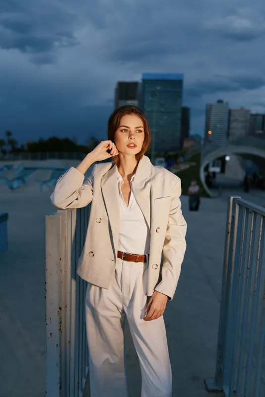 Confident business woman in stylish outfit against urban backdrop, showcasing sophistication and empowerment in a modern setting.