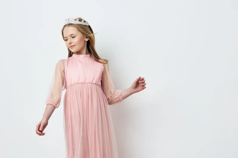 A young girl wearing a pink dress with tulle sleeves poses gracefully against a light background, exuding innocence and beauty, perfect for spring themed photography