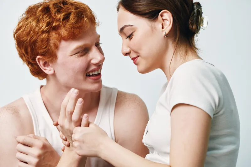 Young couple smiling and holding hands in tender moment, woman and man with red hair expressing affection and connection in casual clothing.