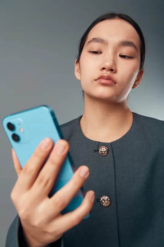 Young woman using smartphone with focus on screen in casual outfit. Female holding mobile phone for communication, technology and social networking with neutral background in portrait style.
