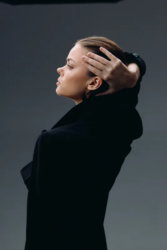 Profile of a contemplative woman with braided hair in black attire, expressing calmness and confidence against a neutral dark background.