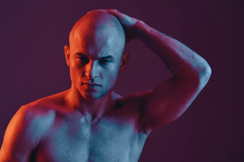 Bald man posing confidently in a striking black and white portrait, showcasing emotion and artistry with dramatic lighting and shadows.