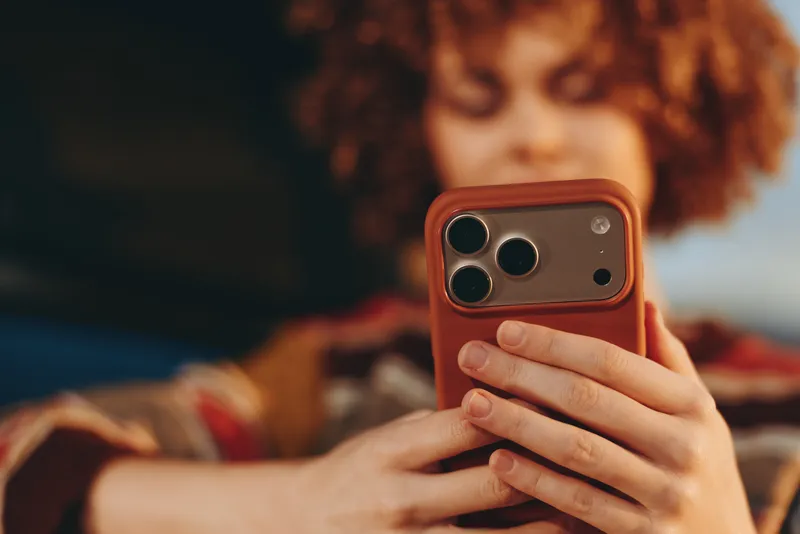 Woman with curly hair taking a selfie with a smartphone, closeup view of hands. Home lifestyle indoors, cozy atmosphere, soft lighting, blurred background and warm mood.