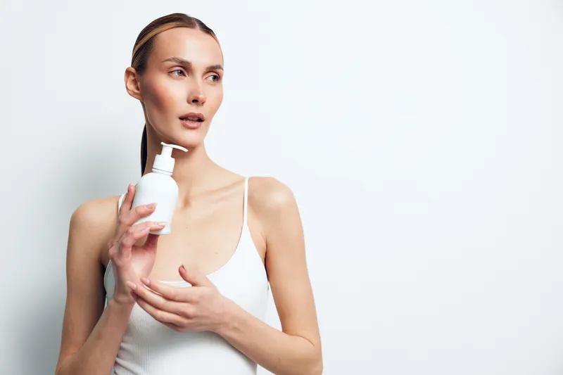 Woman skincare lotion face self care wellness studio white background soft lighting applies moisturizer with hands smiling closeup skincare routine daily care
